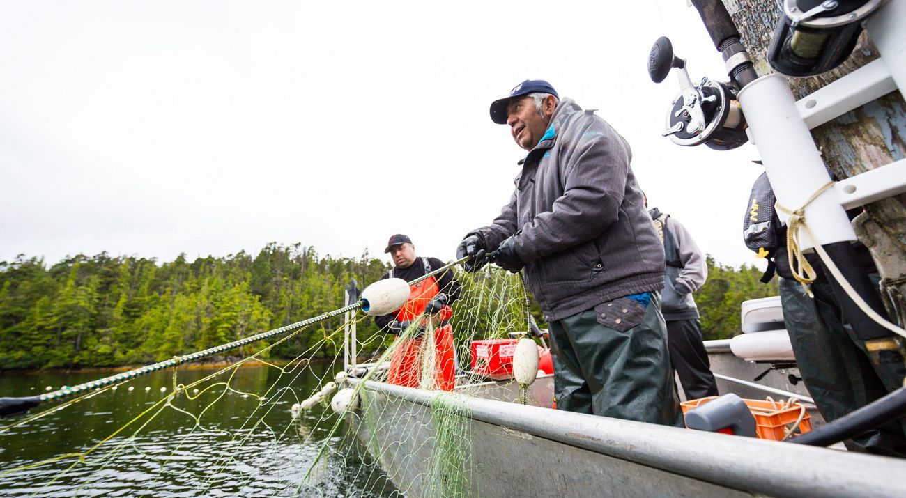 a smiling man standing on a fishing boat pulls a net out of the water