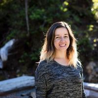 headshot of smiling woman with dark hair in front of green trees