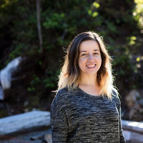 headshot of smiling woman with dark hair in front of green trees