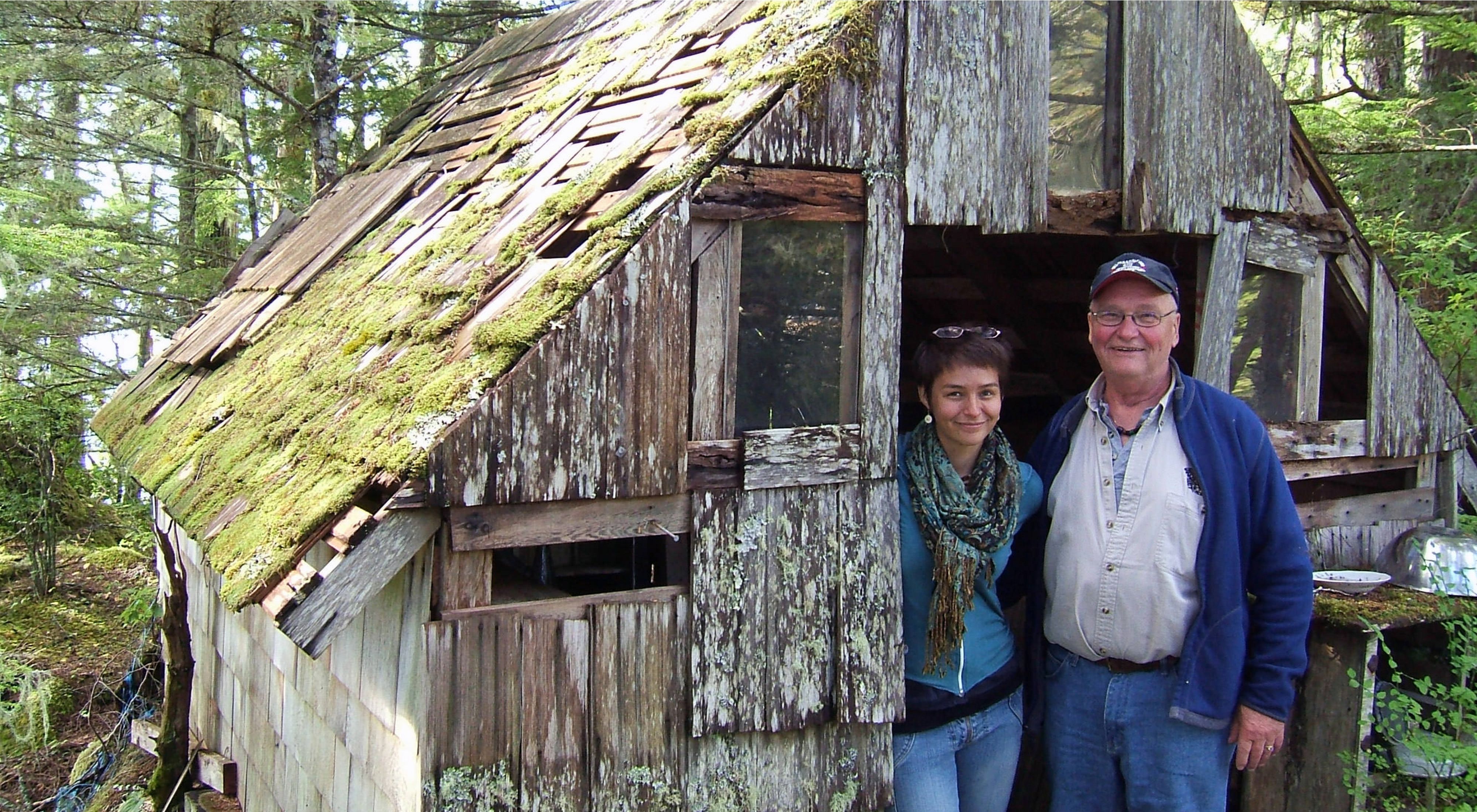 two people standing in the doorway of a small wood cabin