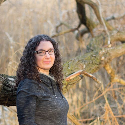 headshot of a woman with curly black hair and glasses