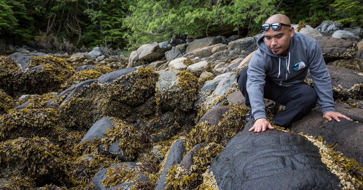 a man in a rocky river bed leaning over a boulder