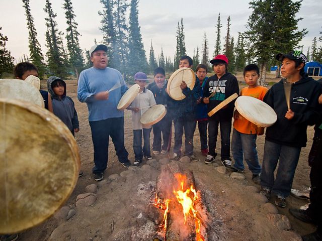 Dene First Nation youth beat drums around a fire during a spiritual gathering after returning from a canoe trip on the Upper Thelon River.