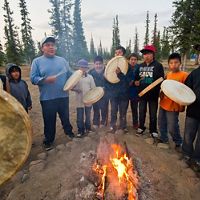 a group of young people stand around a fire while drumming and singing