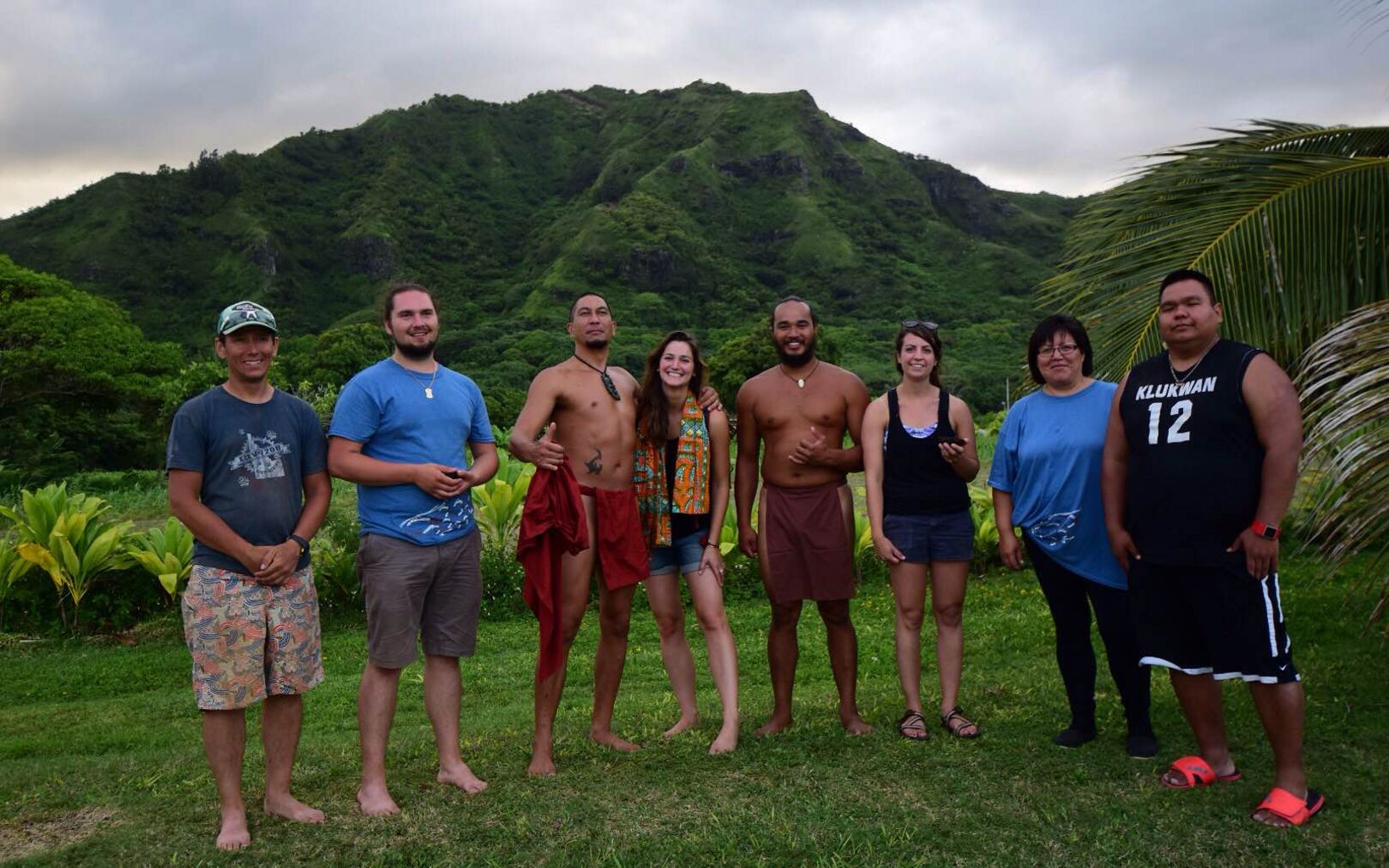 Eight Indigenous people stand for a group photo, with verdant mountains in the background.