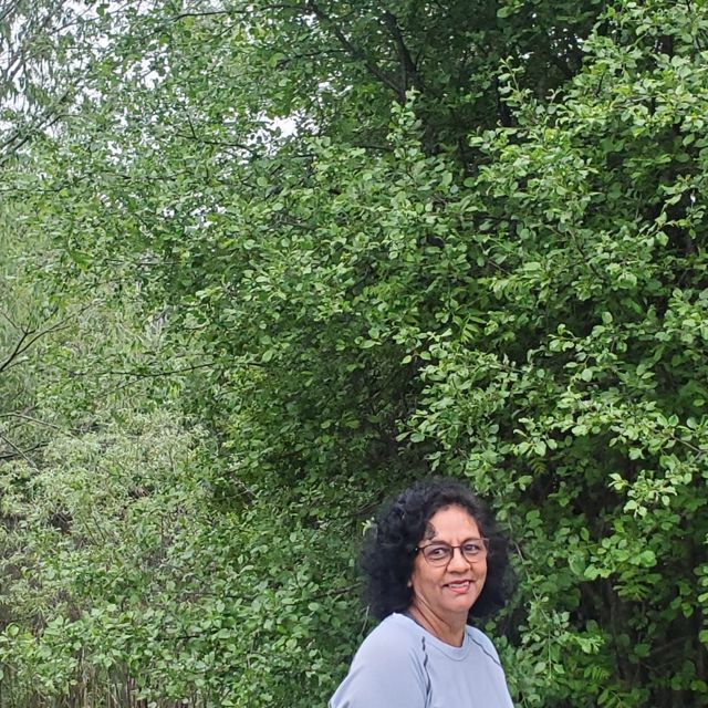woman with glasses smiling and surrounded by trees