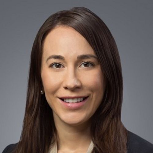 a woman with dark hair smiling in front of a gray background