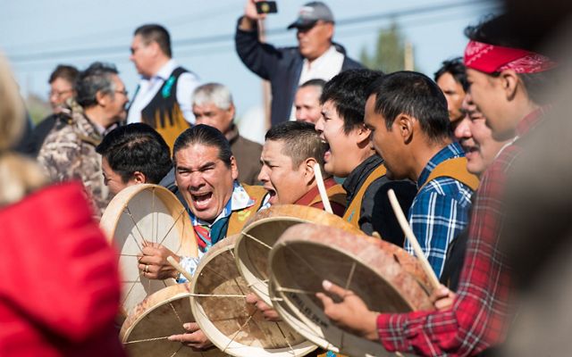 A group of men stand together and bang drums and yell.