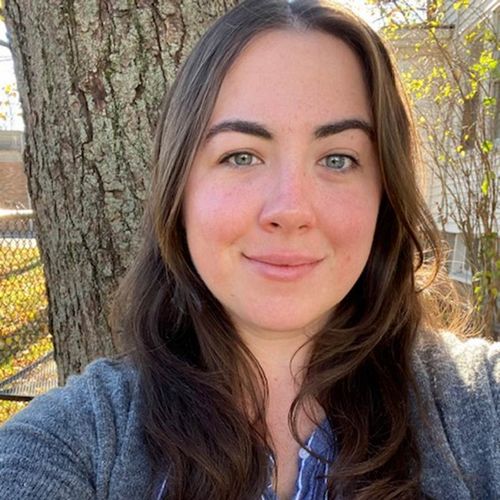 a woman with long dark hair standing in front of a tree