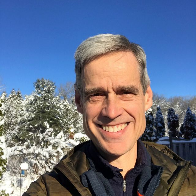a man with gray hair smiling in front of a snowy mountain