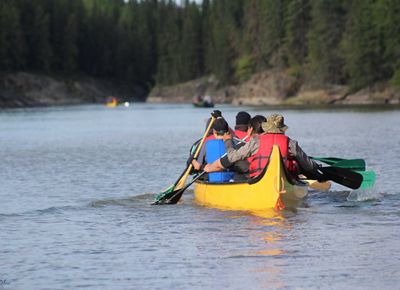 A group of kids and an adult paddling a canoe.