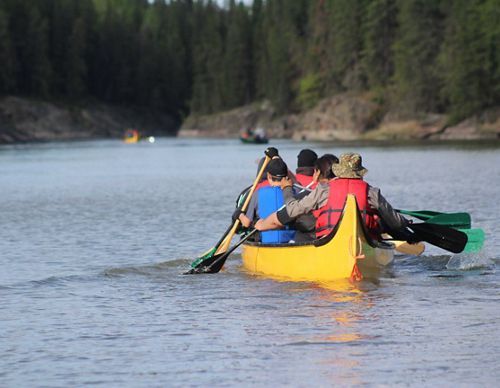 A group of kids and an adult paddling a canoe.