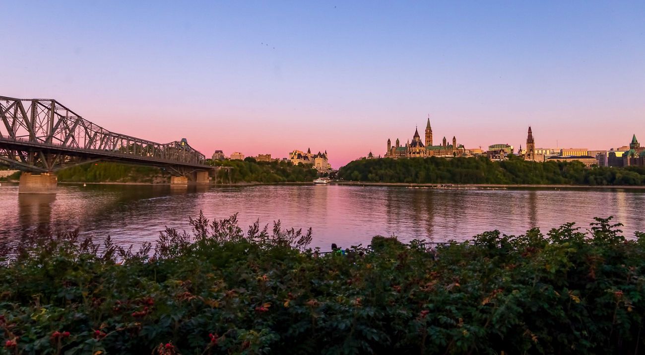 a river and a bridge in front of the canadian parliament building in ottawa