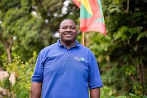 Orlando Harvey smiles as he stands in front of bright green trees.