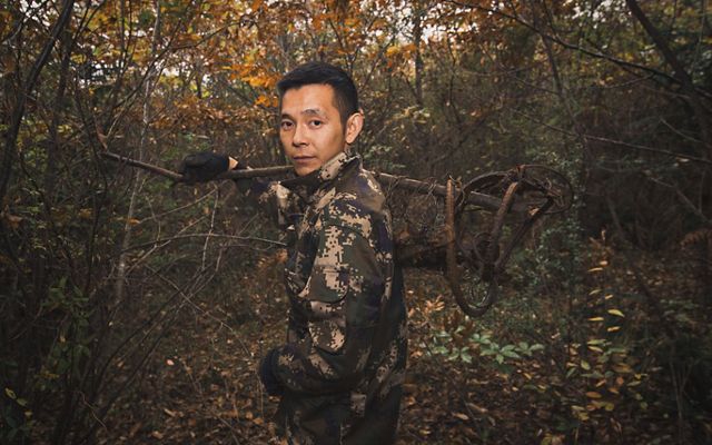 Gan Mingdong stands in a forest and holds a bear trap over his shoulder.