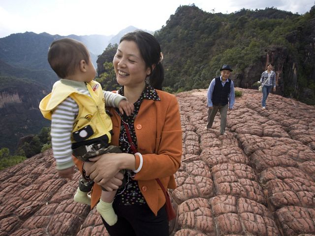 Woman smiling, holding baby walking up mountain