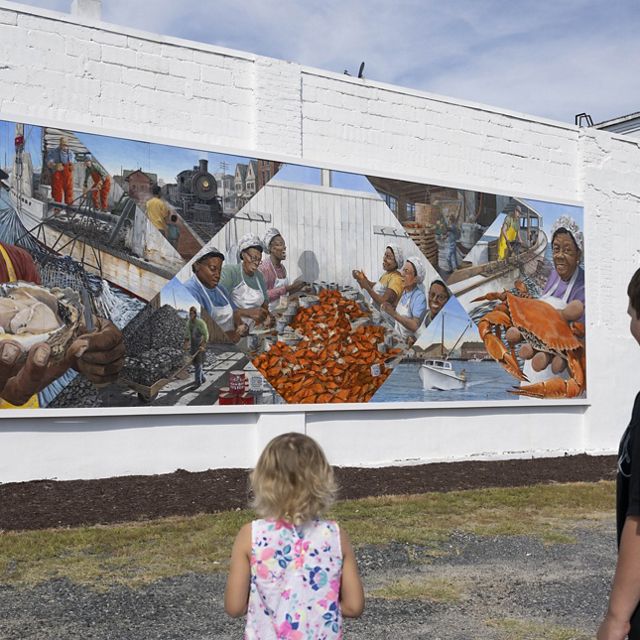 Two young people look at a large mural painted on the wall of a building.