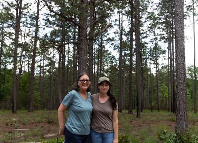 Two women with trees behind them smile at camera.