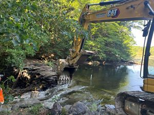 A large yellow piece of digging equipment breaks down a dam on a small pond.
