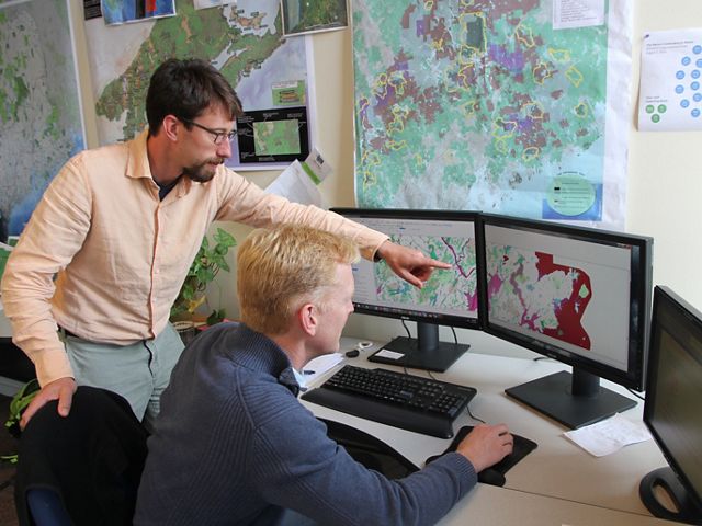 Two people work at a computer with mapping software visible.