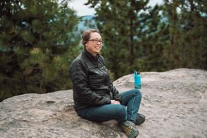 A woman sitting on a big boulder during a hike.