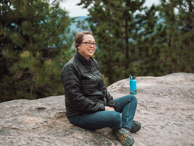 A woman sitting on a boulder during her hike.