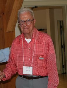 A older man wearing glasses and a red checkered shirt.