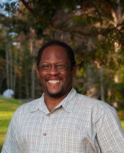 A man wearing glasses with a blurred background of trees