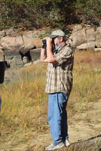 A person wearing a baseball cap looks at something through binoculars.