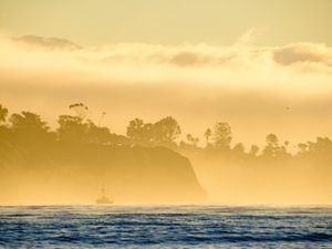 A fishing boat in fog with tall cliffs behind it.