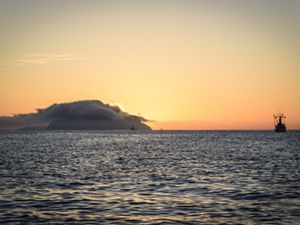 A fishing boat on the ocean during a foggy sunset.