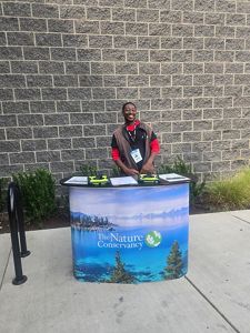 Image of an F2F canvasser smiling while posing behind a Nature Conservancy banner.