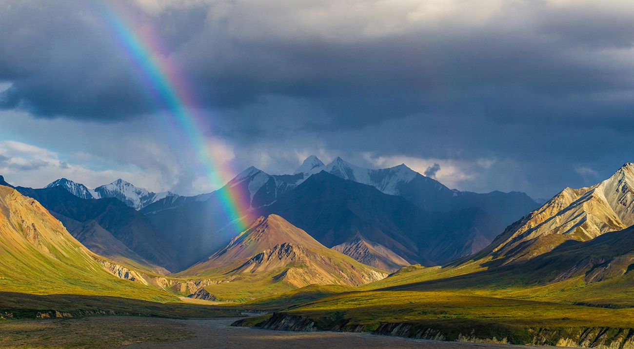 A rainbow stretches over a mountain valley.