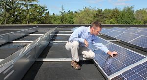 A man crouches down to inspect rooftop solar panels.
