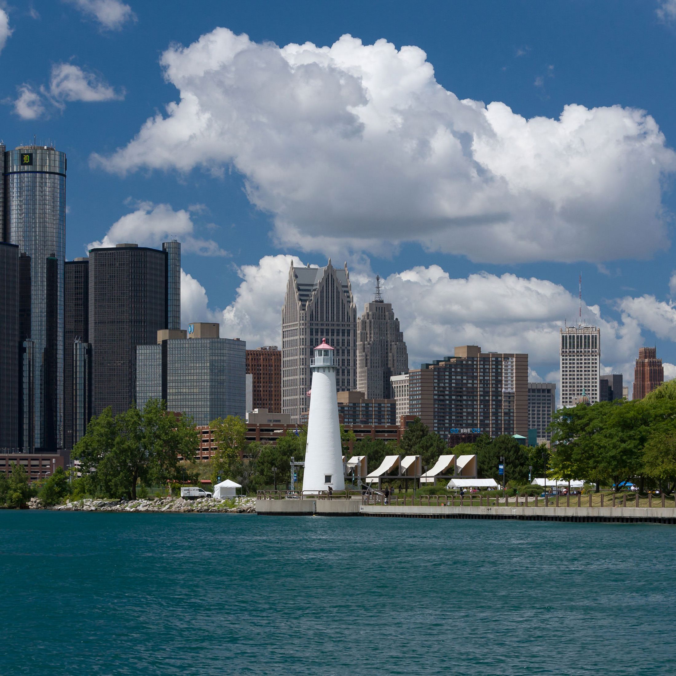 The Detroit, Michigan skyline from the water on a beautiful, sunny day. The sky is bright blue and filled with fluffy, white clouds. 