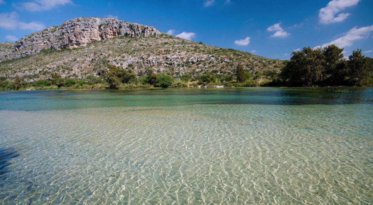 The turquoise waters of a river lined with dense brush ripple and flow.