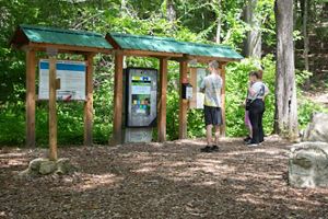 People stand in front of a kiosk surrounded by woods.