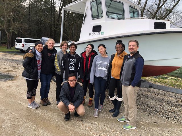 A group of students pose together in front of a boat at Brownsville Preserve's maintenance shop.