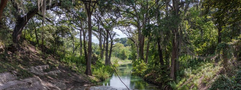A creek meets the edge of large limestone boulders, lined by dense trees.