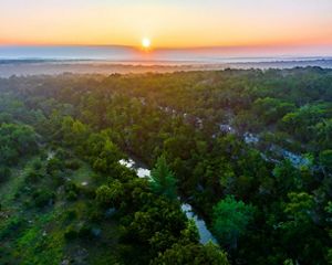 The sun rises over a vast expanse of green brush and a blue river.