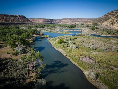 A blue river flowing through shrubs with red mesas in the background.