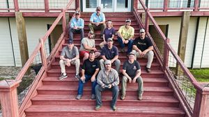 Ten men and one woman sit on red wooden steps.