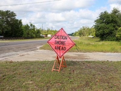 A read caution sign by the side of a road reads "caution smoke ahead."
