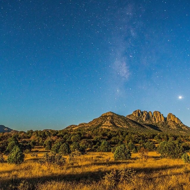 Landscape view of the Davis Mountains in Texas under a darkening night sky; the Milky Way is starting to appear above the craggy mountains.