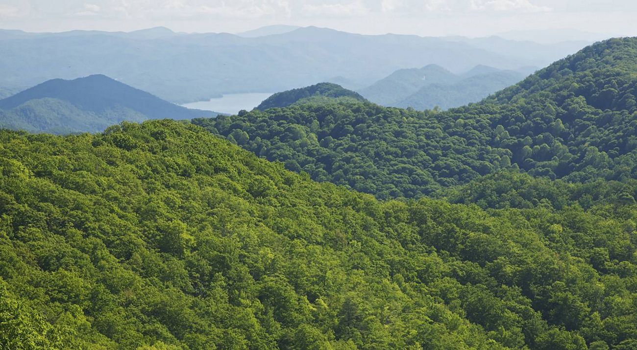Rolling green mountain ridges enclose a mist covered valley. A lake is visible on the valley floor.