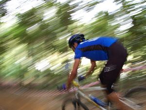 A mountain biker in a blue shirt races past trees.