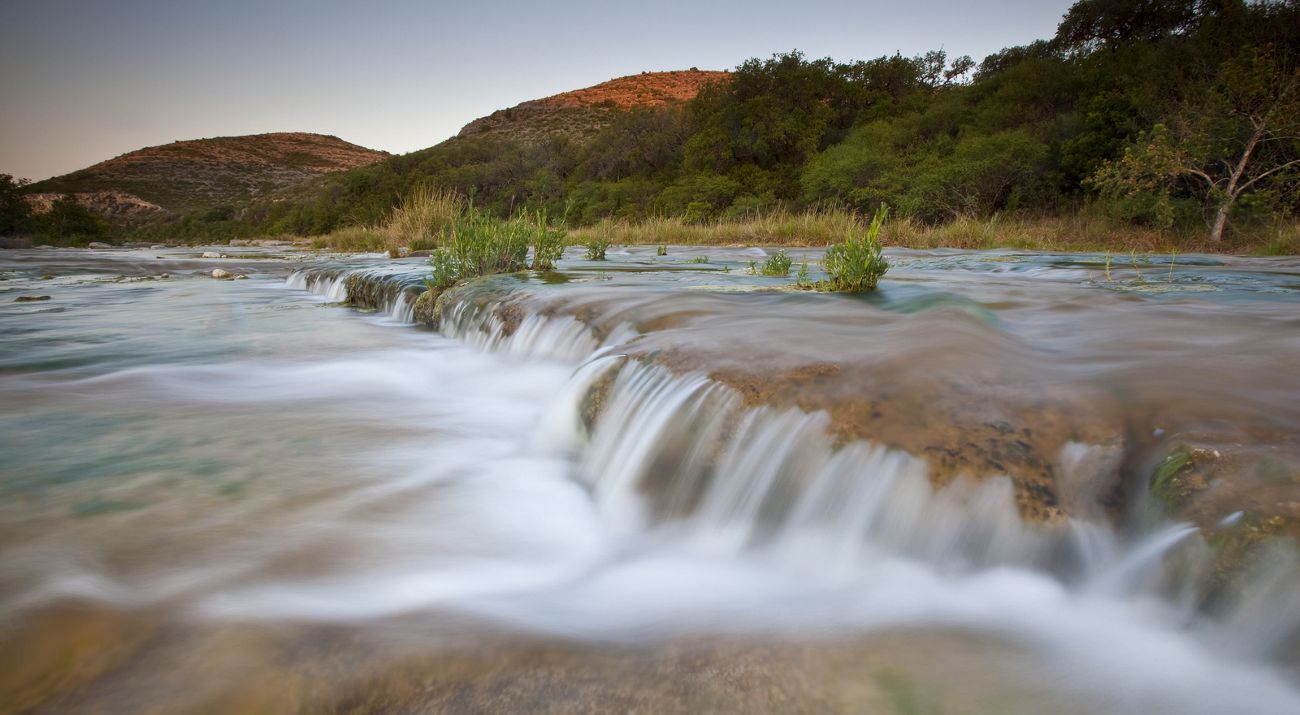 Water flows over limestone boulders lined with dense trees and hills.