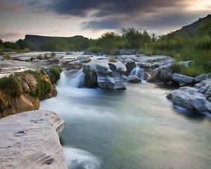 Turquoise waters flow and fall over stacked rocks surrounded by greenery.