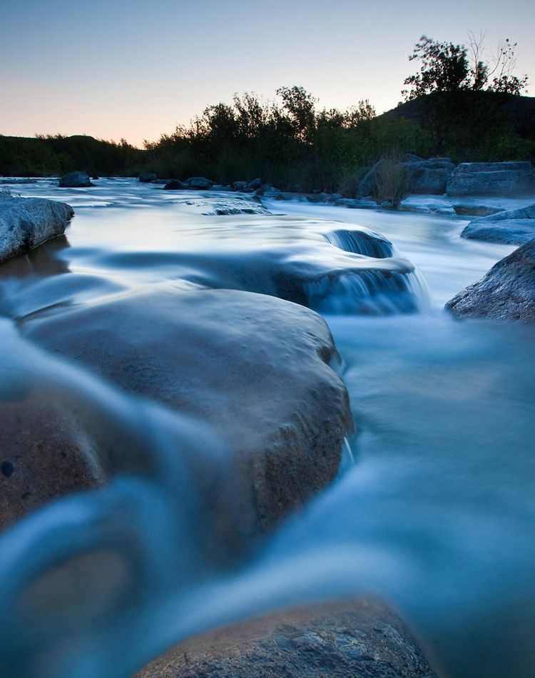 Blue waters flow over large stone boulders.