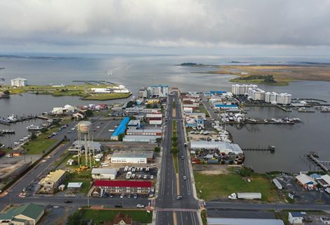 Aerial view of a small coastal community. A four-lane divided road runs through the center of the downtown commercial area surrounded on three sides by the waters and marshes of the Chesapeake Bay.